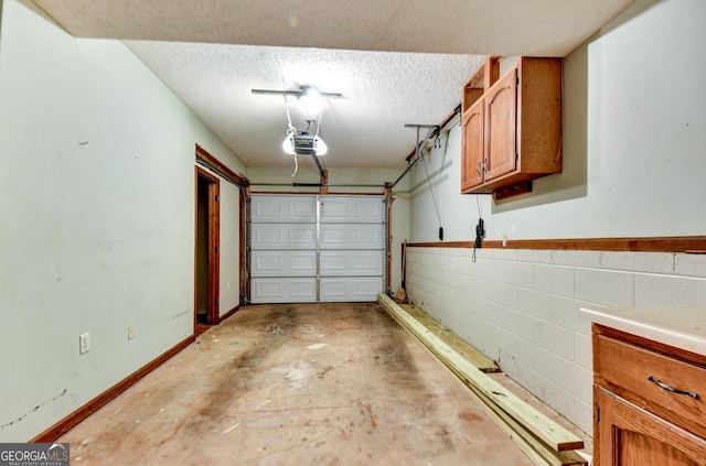 garage with concrete block wall, baseboards, and a garage door opener