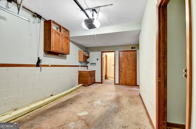 garage with visible vents, baseboards, concrete block wall, and a garage door opener