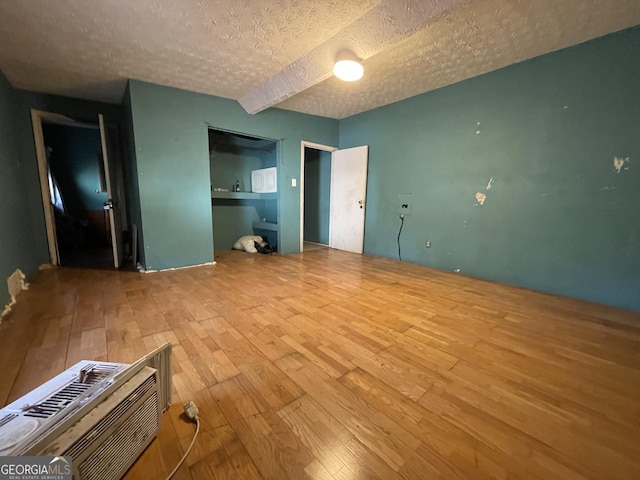 unfurnished bedroom featuring a textured ceiling, a wall mounted air conditioner, and wood finished floors