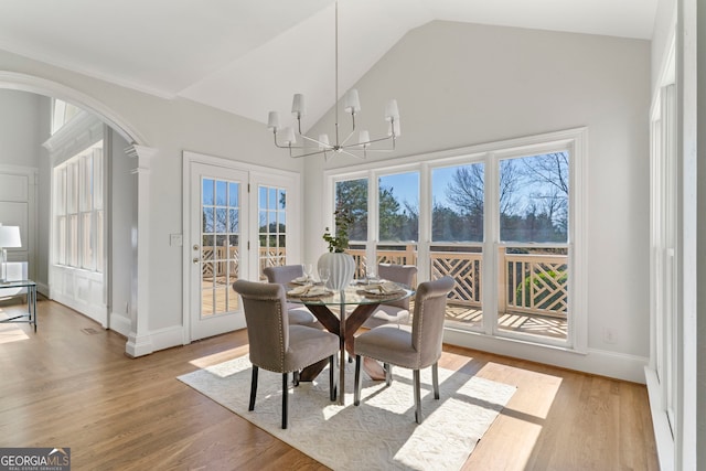 dining room featuring light wood finished floors, baseboards, arched walkways, high vaulted ceiling, and a notable chandelier