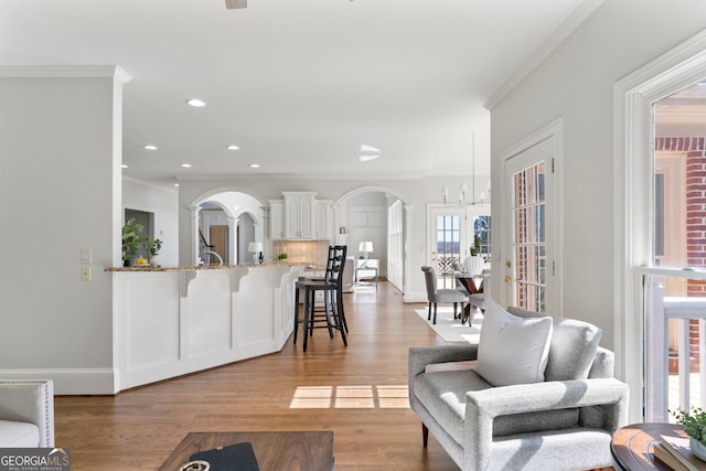 living area with arched walkways, crown molding, recessed lighting, light wood-style floors, and baseboards