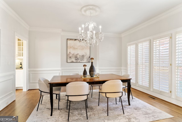 dining area with light wood-type flooring, crown molding, visible vents, and a notable chandelier