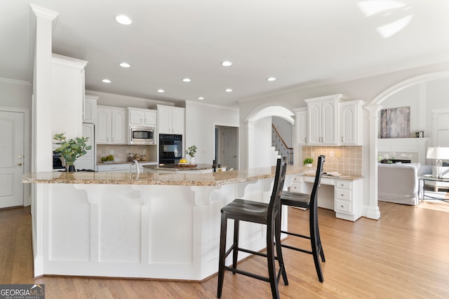 kitchen featuring oven, stainless steel microwave, light wood finished floors, and white cabinetry