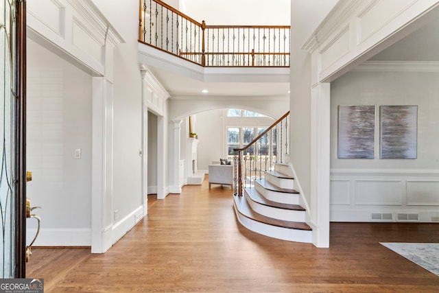 foyer with arched walkways, a decorative wall, ornamental molding, stairway, and light wood-type flooring