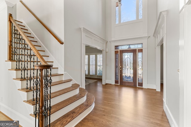 foyer entrance featuring baseboards, stairway, a high ceiling, and wood finished floors