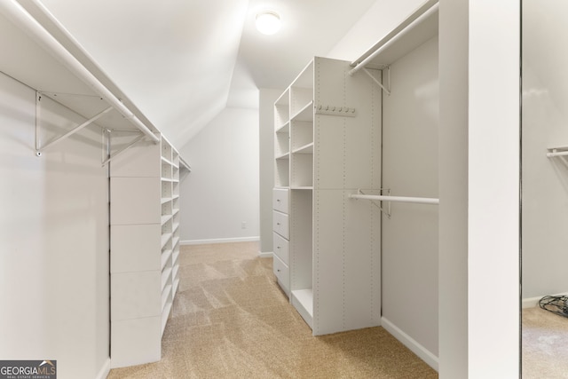 walk in closet with vaulted ceiling and light colored carpet