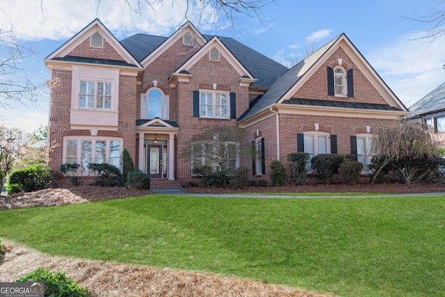 view of front of property featuring brick siding, a front lawn, and roof with shingles