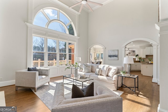 living room with arched walkways, ornamental molding, decorative columns, and light wood-style flooring