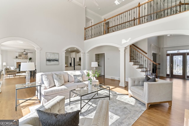 living room with stairway, decorative columns, arched walkways, and wood finished floors