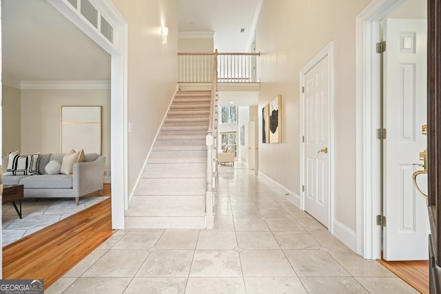 entryway with light tile patterned flooring, a high ceiling, baseboards, stairway, and crown molding