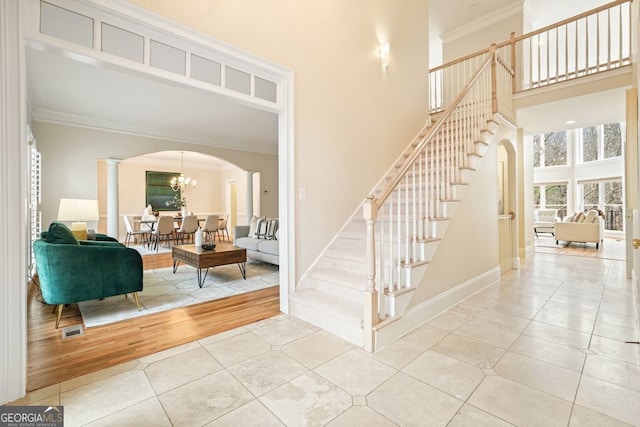 tiled entryway featuring arched walkways, a notable chandelier, a high ceiling, stairs, and crown molding