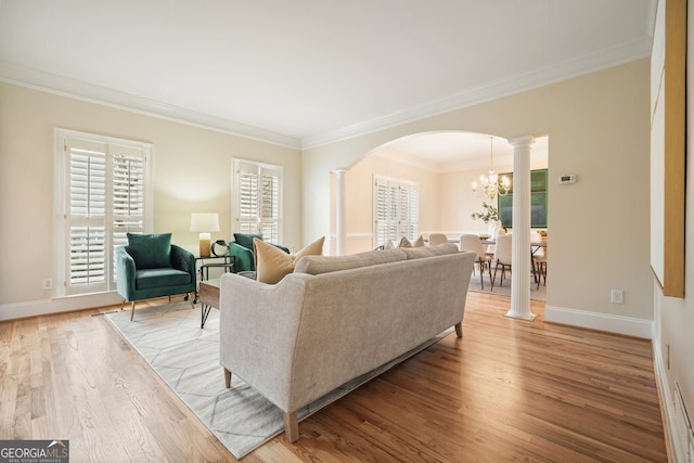 living area featuring arched walkways, a chandelier, ornamental molding, light wood finished floors, and decorative columns