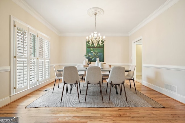 dining area with a chandelier, ornamental molding, wood finished floors, and visible vents