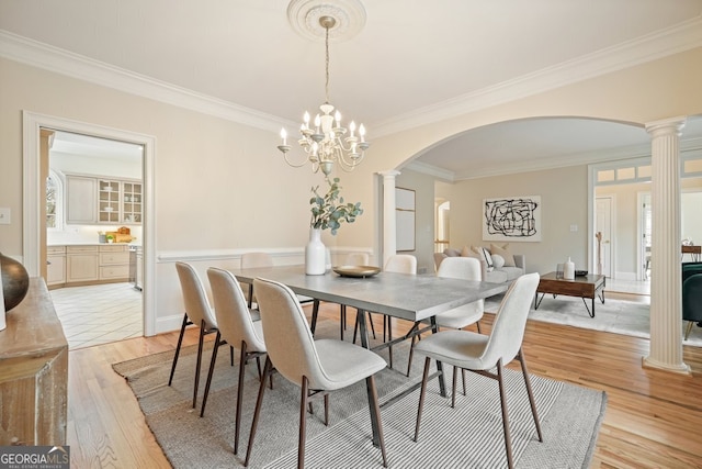 dining room with ornate columns, crown molding, arched walkways, and light wood-style floors