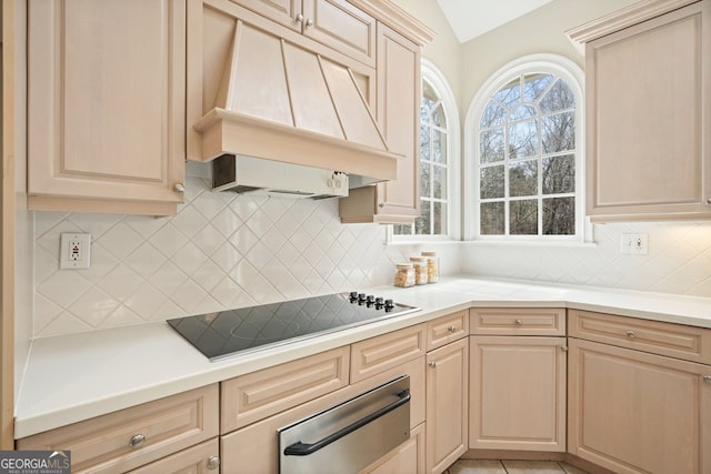 kitchen with light brown cabinets, custom range hood, black electric stovetop, and a warming drawer