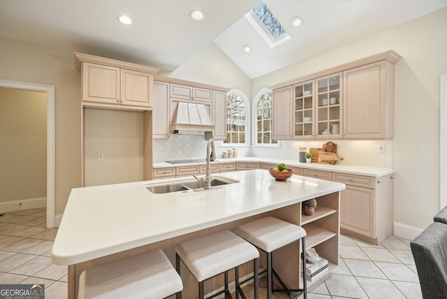 kitchen featuring glass insert cabinets, light tile patterned flooring, a sink, vaulted ceiling with skylight, and premium range hood