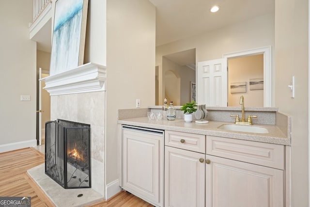 bathroom featuring double vanity, baseboards, a tile fireplace, wood finished floors, and a sink