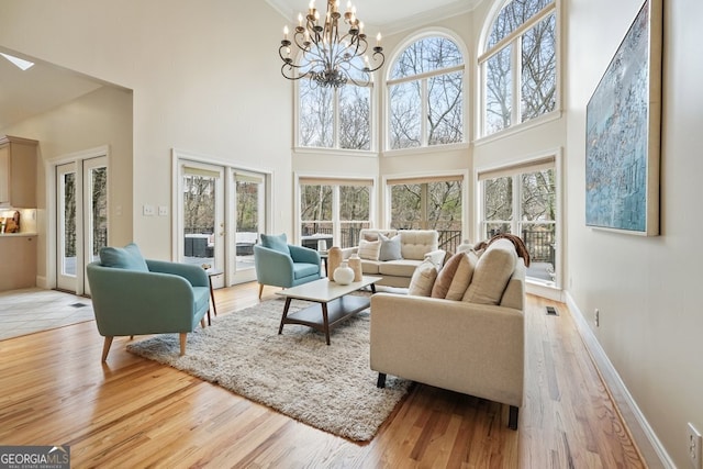 living area featuring french doors, a high ceiling, light wood-style floors, a chandelier, and baseboards