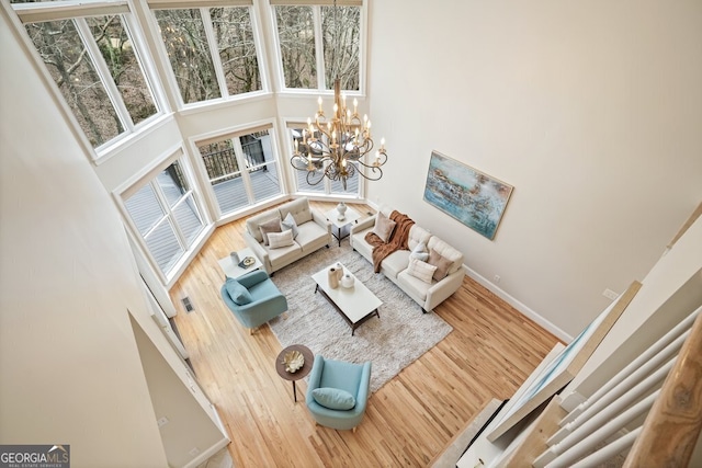 living area featuring an inviting chandelier, baseboards, a high ceiling, and wood finished floors