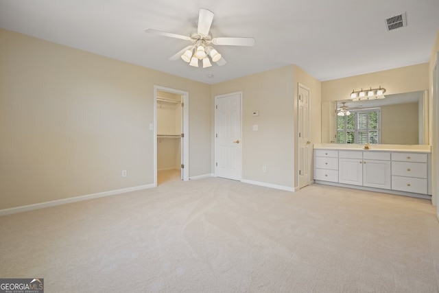 unfurnished bedroom with light carpet, baseboards, visible vents, a ceiling fan, and a walk in closet