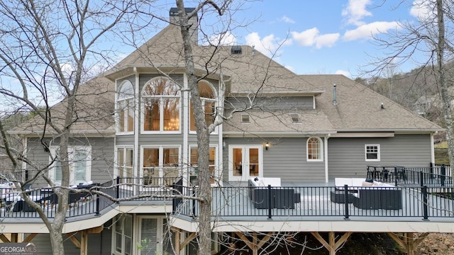 rear view of property with a shingled roof, french doors, a chimney, and a deck