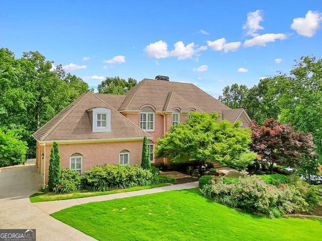 view of front of home with driveway, a chimney, a front lawn, and brick siding