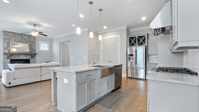 kitchen featuring a stone fireplace, under cabinet range hood, wood finished floors, a sink, and appliances with stainless steel finishes