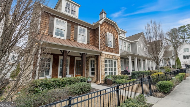 view of front facade featuring metal roof, a porch, a fenced front yard, a standing seam roof, and a chimney