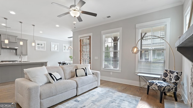 living area featuring light wood-style floors, a ceiling fan, baseboards, and crown molding