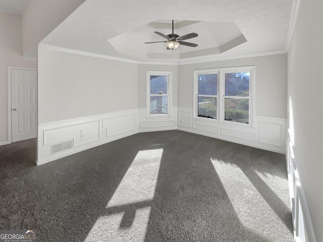 empty room with plenty of natural light, visible vents, dark carpet, and a tray ceiling