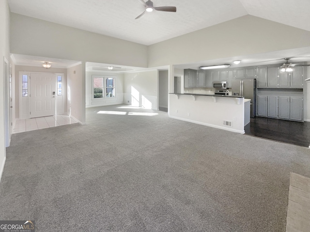 unfurnished living room featuring lofted ceiling, visible vents, dark colored carpet, and a ceiling fan