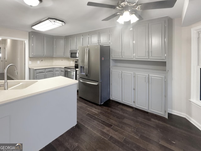 kitchen featuring dark wood-style floors, stainless steel appliances, light countertops, gray cabinetry, and a sink