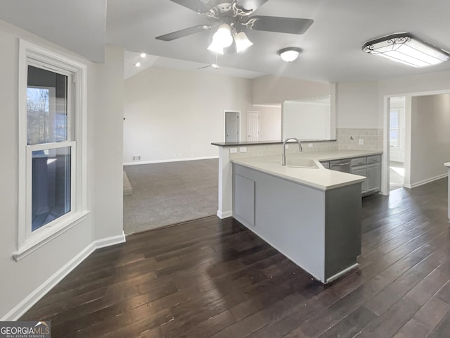 kitchen featuring dark wood-style flooring, decorative backsplash, a sink, dishwasher, and a peninsula