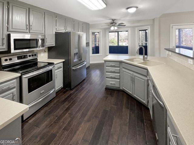 kitchen featuring dark wood-style flooring, stainless steel appliances, gray cabinets, light countertops, and a sink