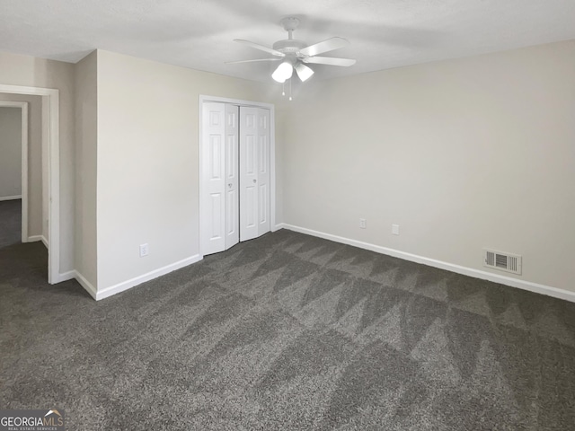 unfurnished bedroom with a closet, visible vents, dark carpet, and baseboards