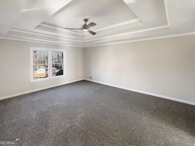 spare room featuring a ceiling fan, a tray ceiling, dark carpet, and baseboards