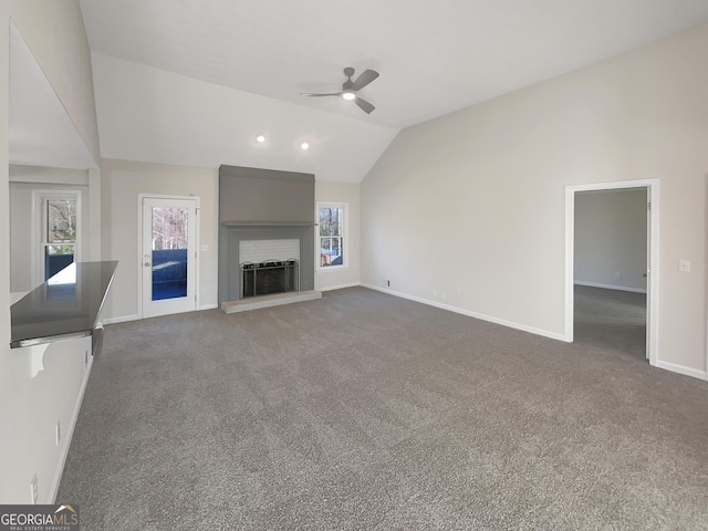 unfurnished living room with plenty of natural light, lofted ceiling, carpet flooring, and a fireplace with raised hearth