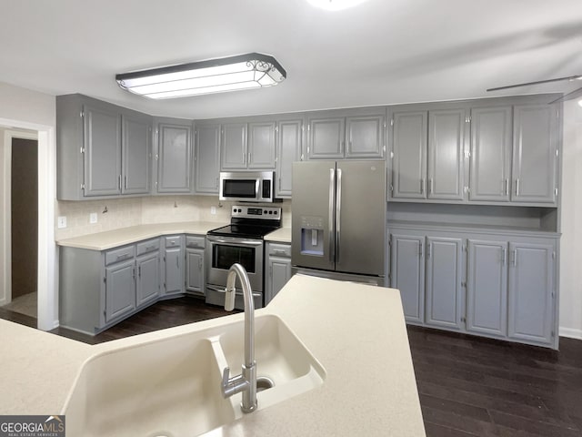 kitchen featuring dark wood-type flooring, light countertops, stainless steel appliances, gray cabinetry, and a sink