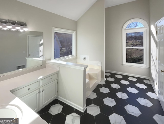 bathroom with a garden tub, vanity, visible vents, vaulted ceiling, and baseboards