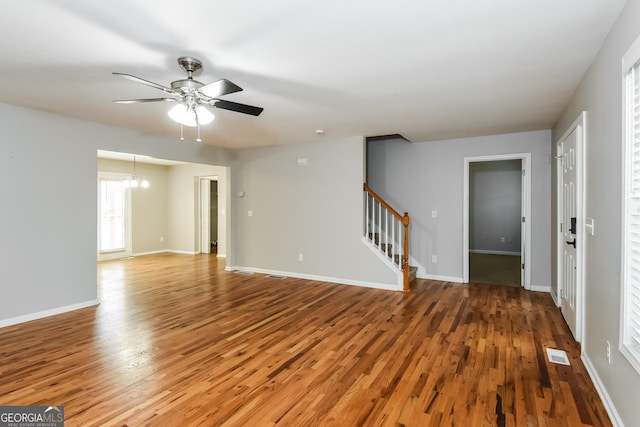 spare room featuring baseboards, visible vents, stairs, light wood-style floors, and ceiling fan with notable chandelier