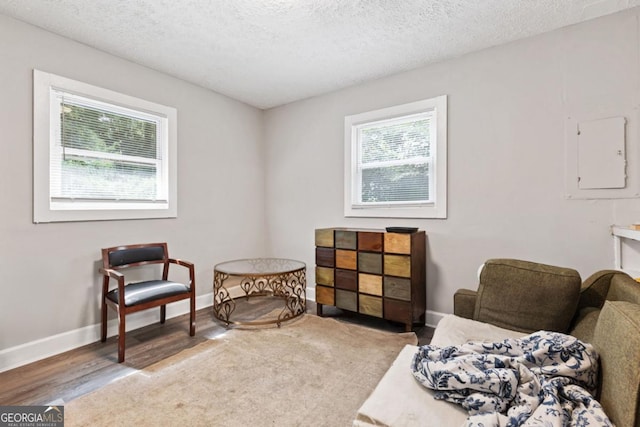 living area with electric panel, baseboards, a textured ceiling, and wood finished floors