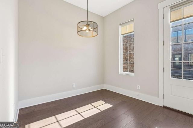 unfurnished room featuring a wealth of natural light, baseboards, dark wood-style flooring, and an inviting chandelier