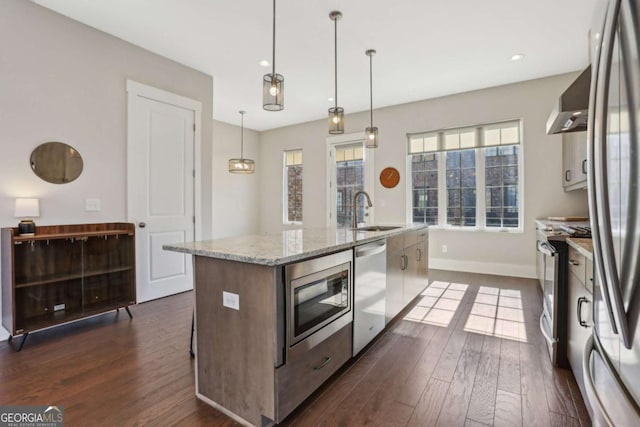 kitchen featuring stainless steel appliances, dark wood-style flooring, a sink, wall chimney exhaust hood, and a center island with sink