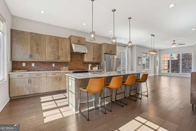 kitchen featuring decorative backsplash, wood-type flooring, freestanding refrigerator, under cabinet range hood, and a sink