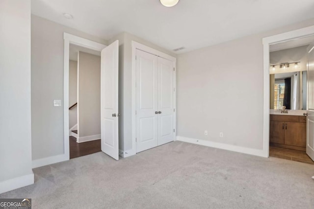 unfurnished bedroom featuring ensuite bathroom, a sink, baseboards, a closet, and carpet