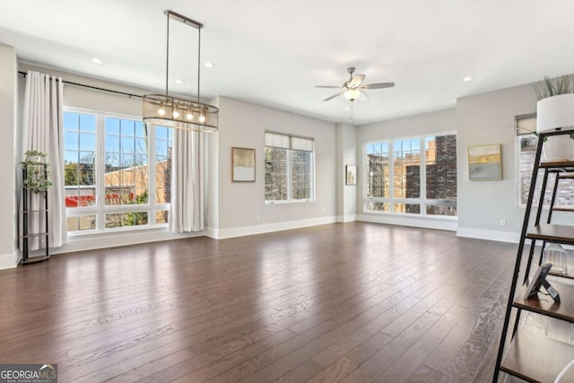 unfurnished living room featuring ceiling fan, dark wood-style flooring, a wealth of natural light, and baseboards