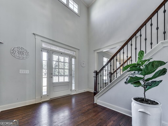 foyer entrance featuring wood finished floors, a towering ceiling, baseboards, stairs, and crown molding