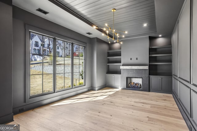 unfurnished living room featuring built in shelves, a fireplace, a notable chandelier, visible vents, and light wood-style floors