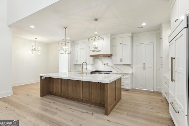 kitchen featuring light wood-type flooring, tasteful backsplash, visible vents, and a sink