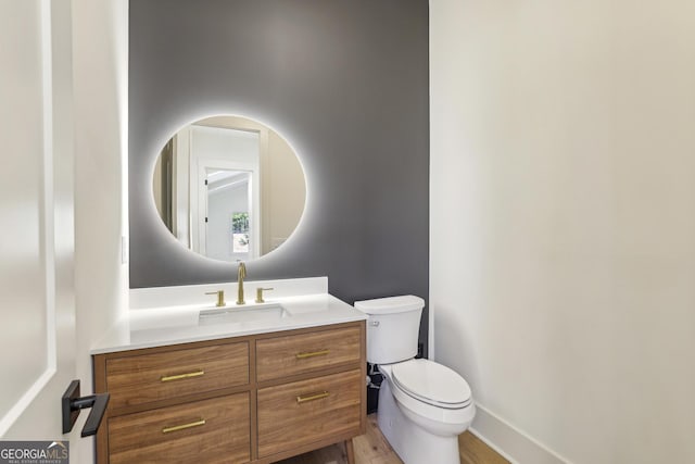 half bath featuring wood finished floors, vanity, toilet, and baseboards